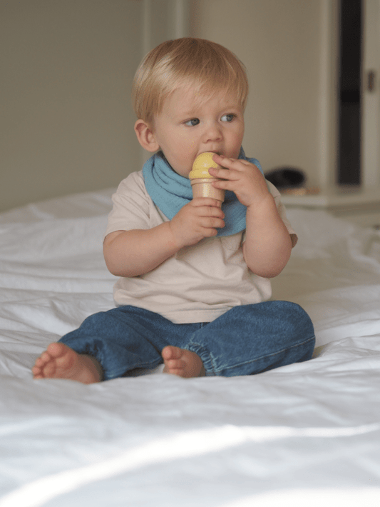 Boy model wearing Blue dribble bib holding ice cream on bed